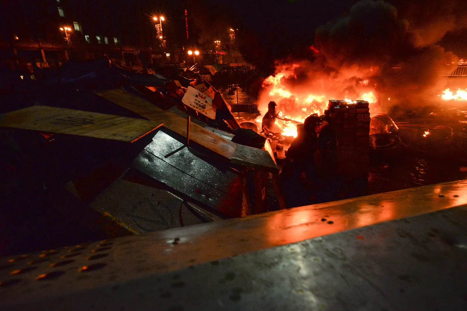 Wooden barricades burn on Independence Square in Kyiv on the night of 18 February 2014, with smoke and sparks above the square.