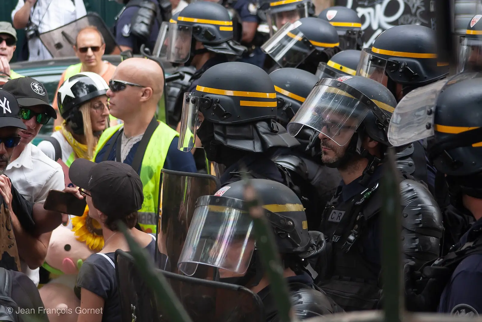 A French riot officer in helmet and visor stands close to a person in a yellow vest on a Paris street, 20 July 2019.