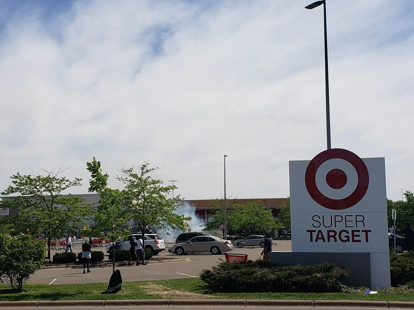 White smoke drifts across a car park in St. Paul, Minnesota, on 28 May 2020, with a few people standing near a shop sign.